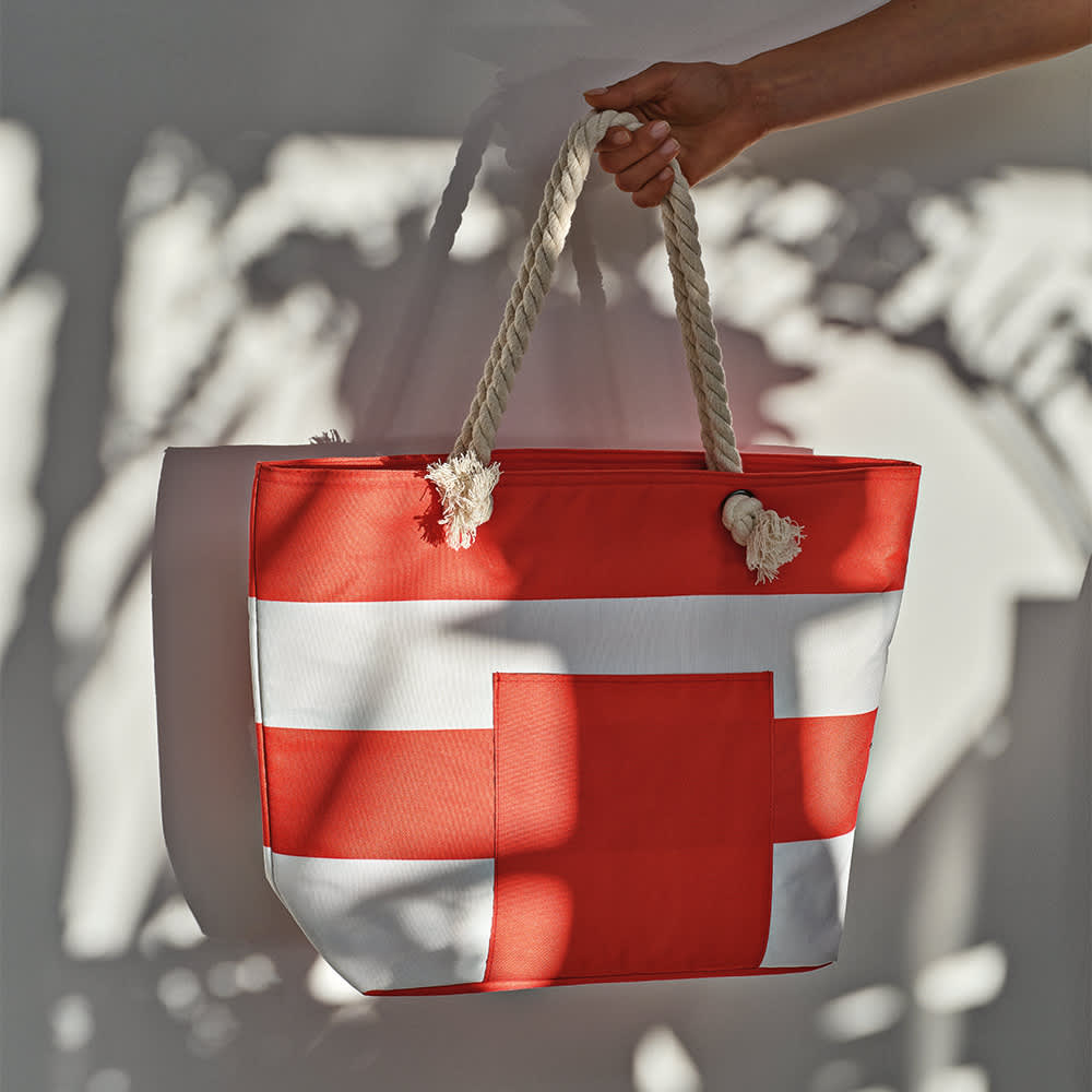 A large red tote bag with white stripes and braided handles, featuring a logo.