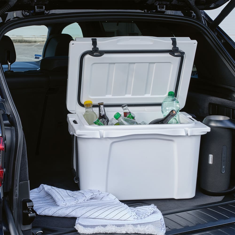 A white cooler with a lid is open in a vehicle, containing various bottles and a towel inside.