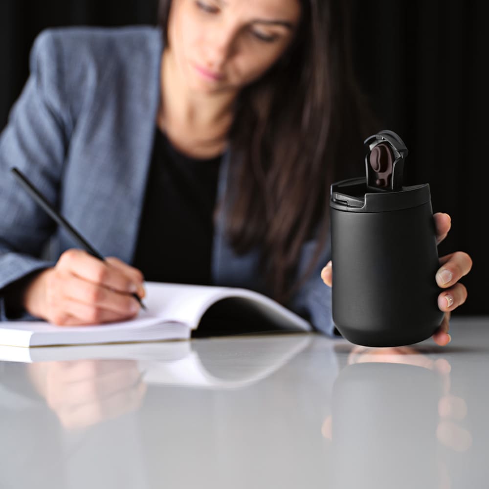 A drink bottle in matte black, featuring a double wall and leakproof design, held by a person writing.