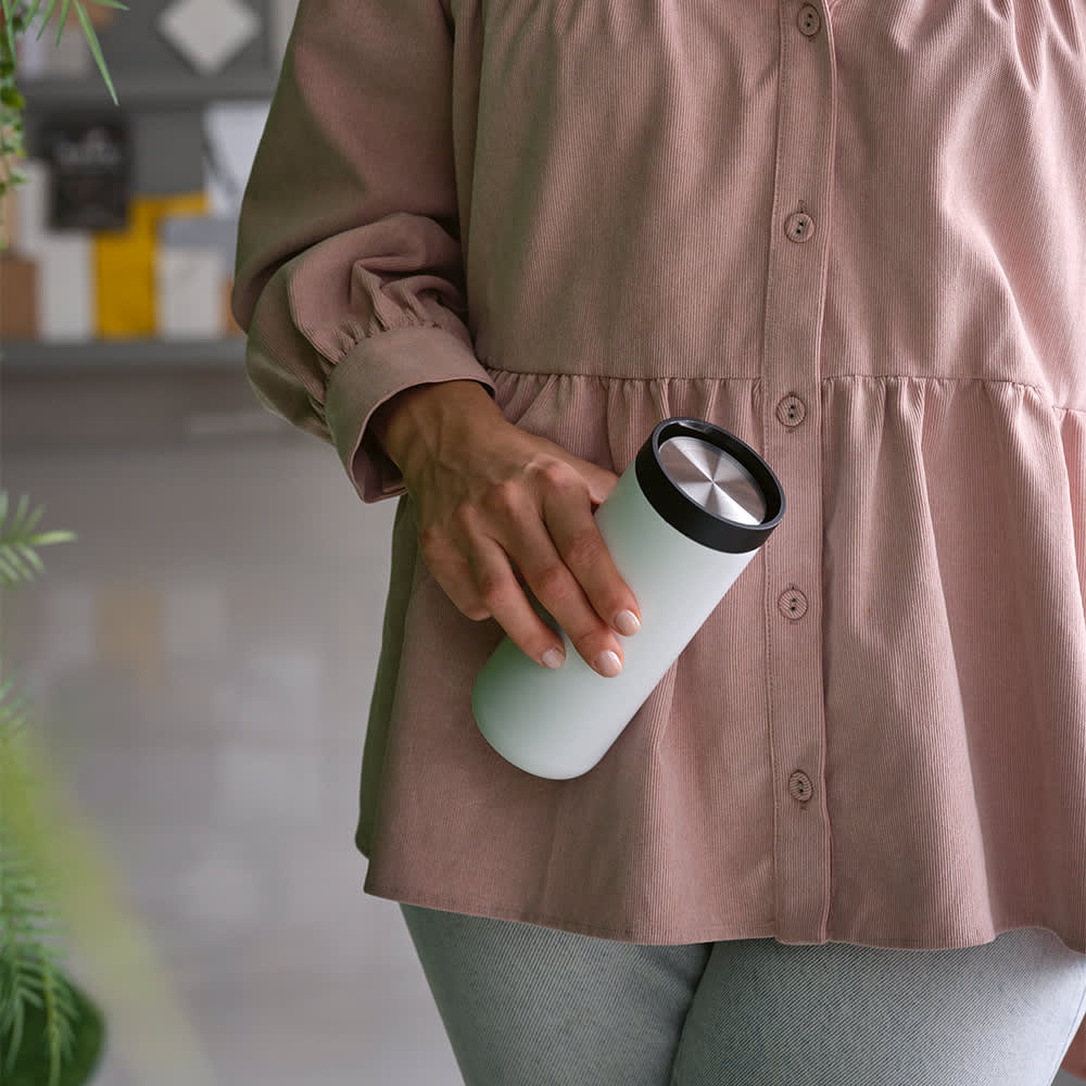 A drink bottle in white with a black lid, held by a person in a soft pink top.