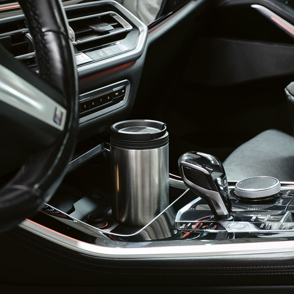 A drink bottle with a double wall design, in silver, placed in a car cup holder with a sleek interior.