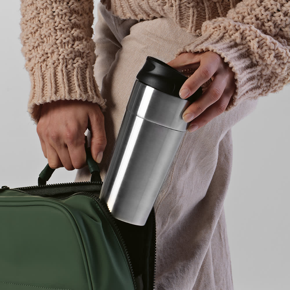 A drink bottle with a silver body, double wall insulation, and a sliding lid, being placed into a bag.