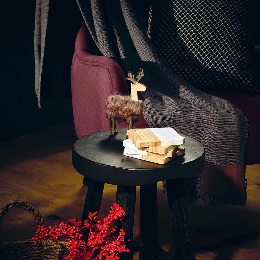 A set of four marble and bamboo coasters rests on a black table, accompanied by a decorative reindeer and berry accents.