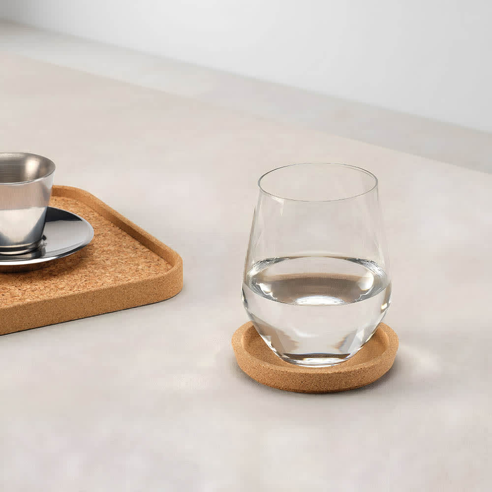 A cork coaster with a rim in natural colour, featuring a glass of water and a stainless steel cup on a tray.