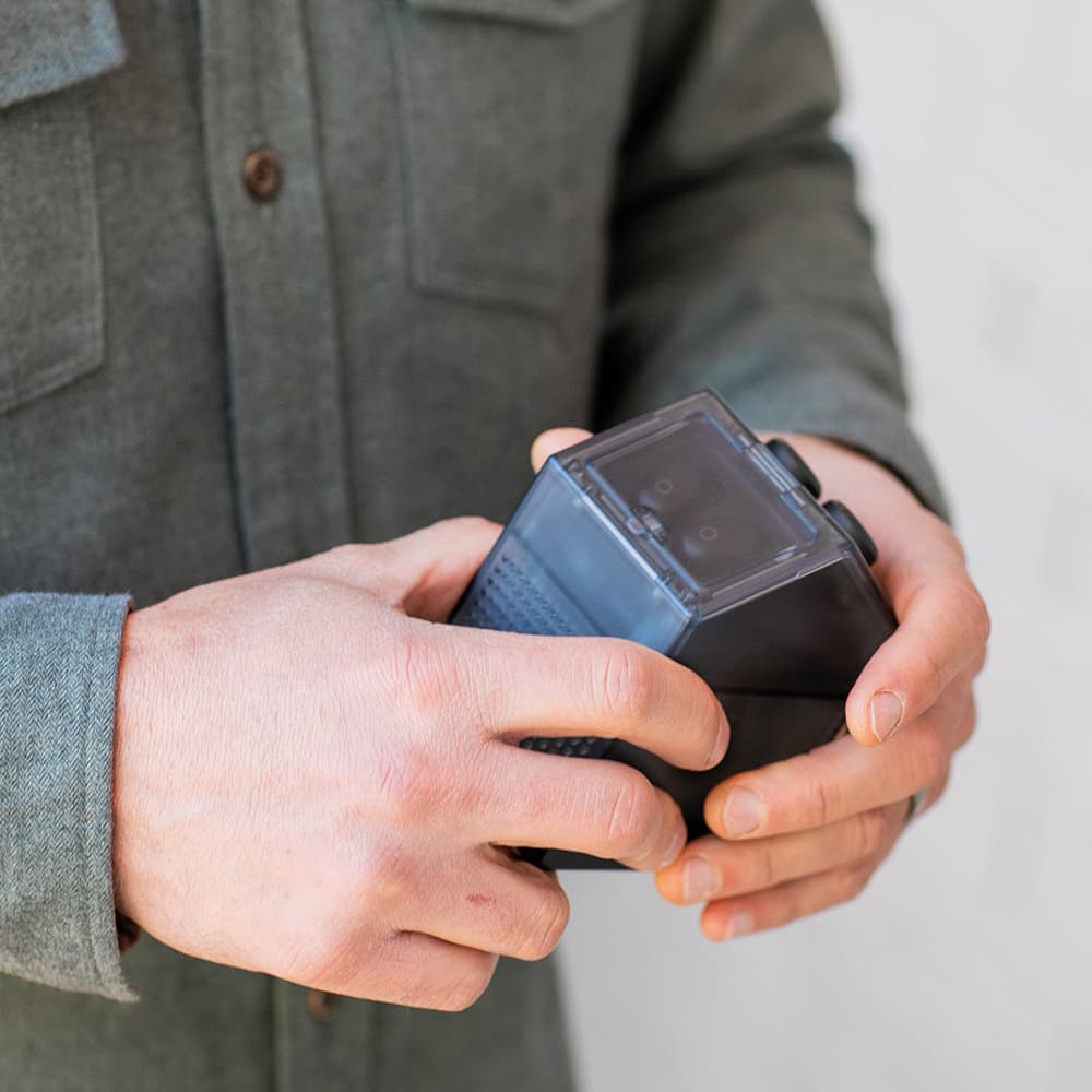A person holds a black, angular device featuring buttons and a transparent top.