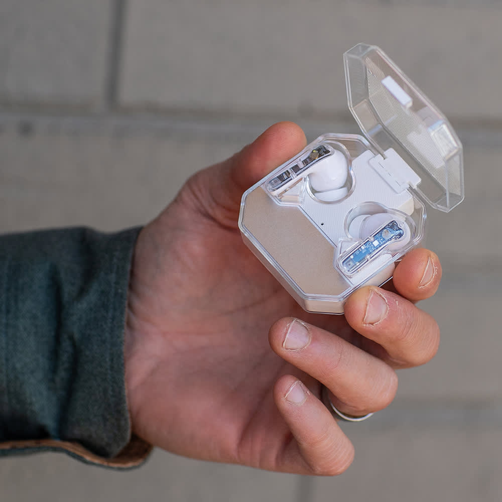A person holding a transparent case with white earbuds inside. The case is octagonal in shape.