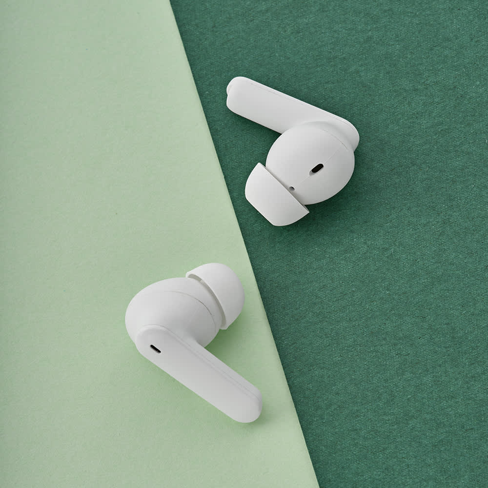 White earbuds positioned on a green background, showcasing their sleek design and charging features.