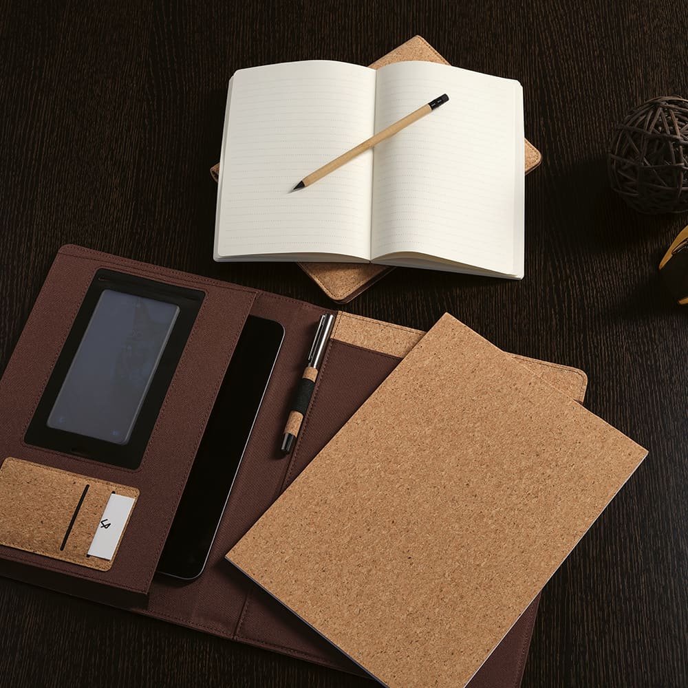 A cork A4 folder in brown, featuring a notepad, pen, and elastic closure, laid on a dark wooden surface.