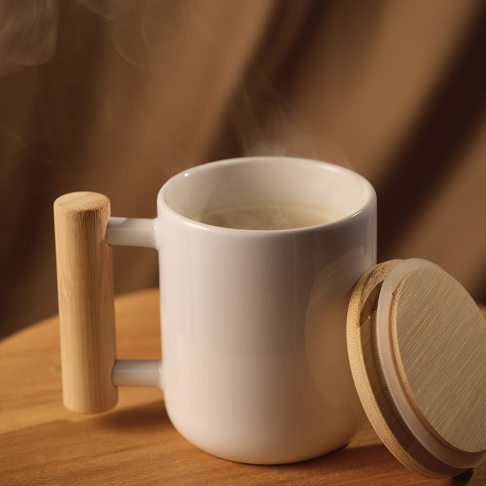A ceramic mug in white with a bamboo lid and handle, featuring steam rising from the opening.