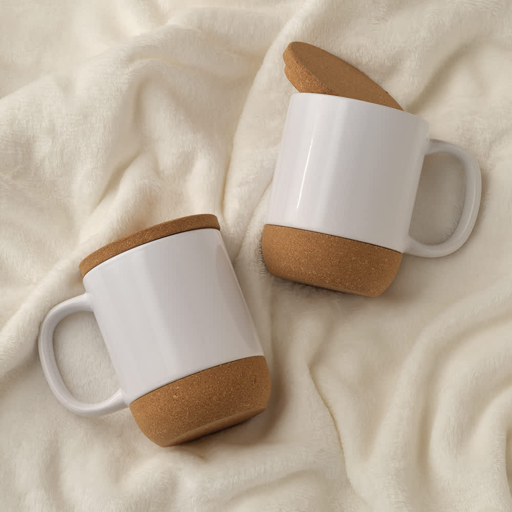 A ceramic mug with a white body and cork lid and base, featuring two mugs on a soft surface.