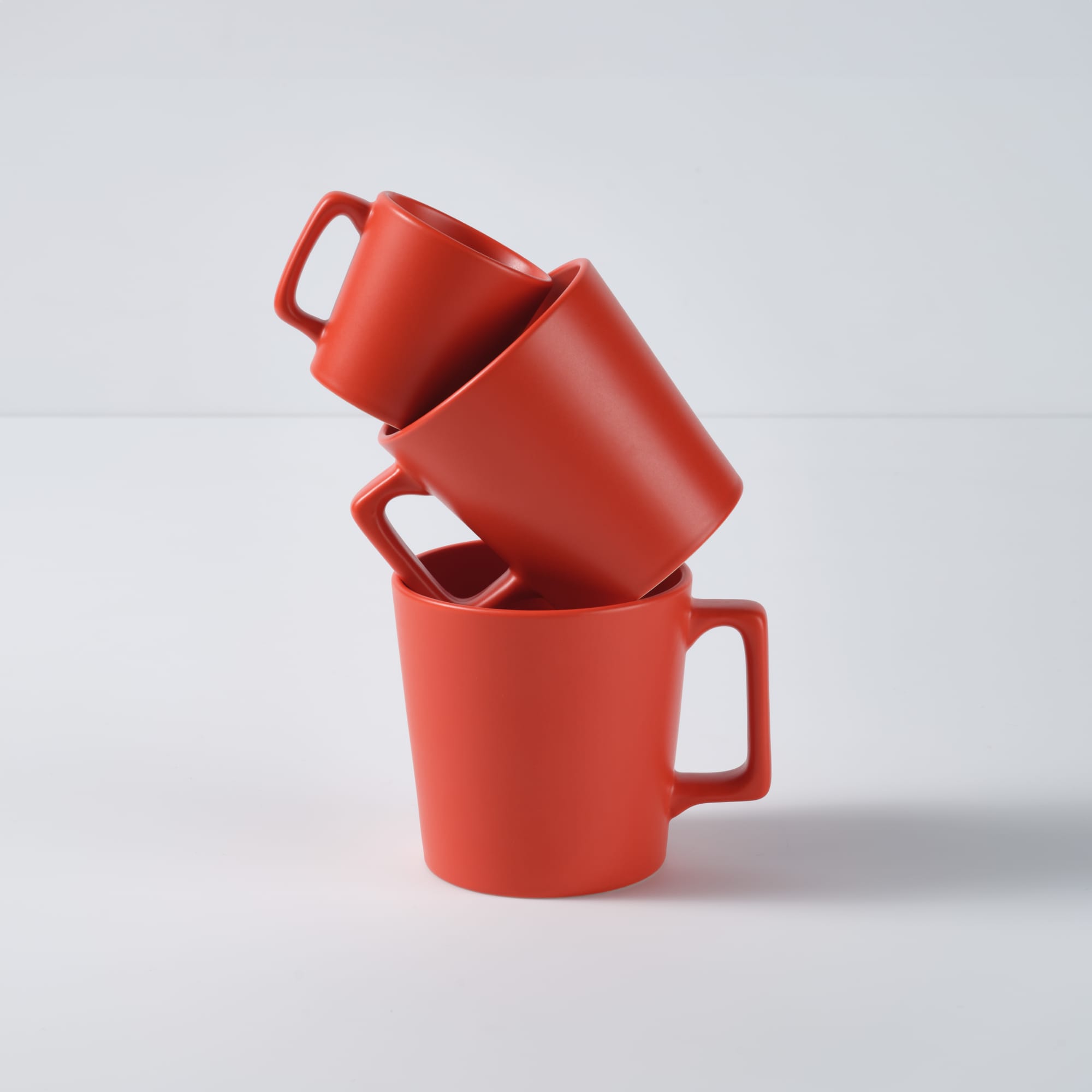 A stack of three red ceramic mugs with matt finish, featuring a handle on each mug.