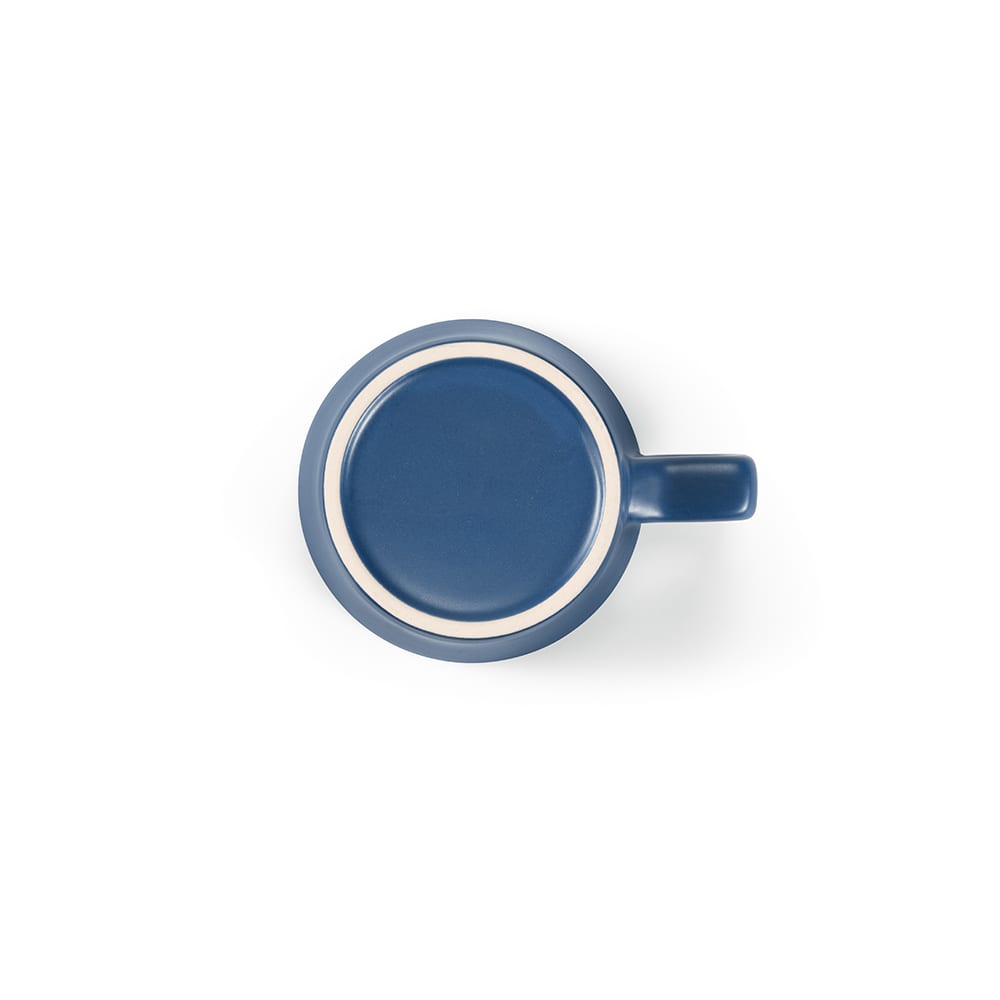 A ceramic mug with a matte finish, featuring a navy blue exterior and white inner rim. It has a handle and a smooth surface.