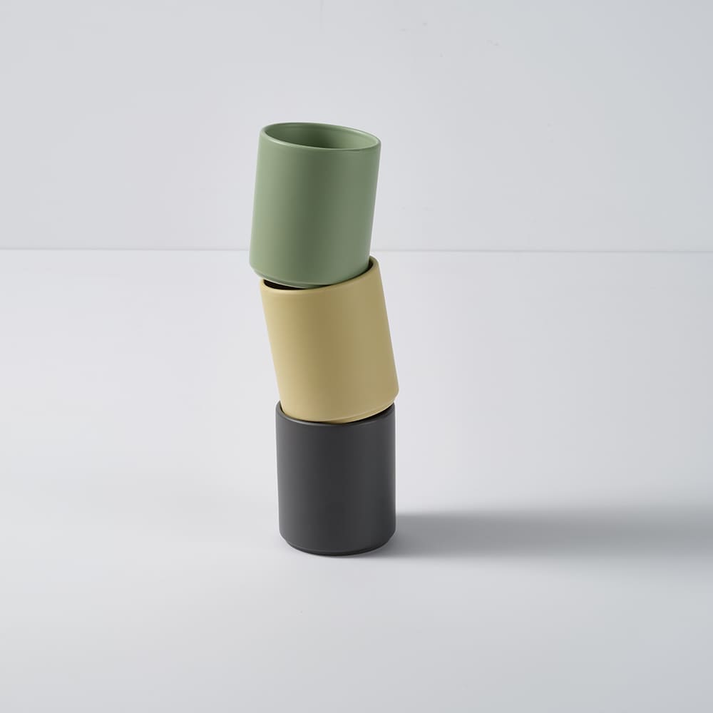 A stack of three ceramic mugs in green, yellow, and black with a matte finish. Each mug has a logo.