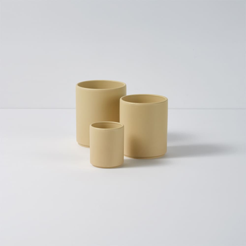 Three ceramic mugs in various sizes, featuring a matte finish in a soft beige colour. Each mug has a simple design and branding.