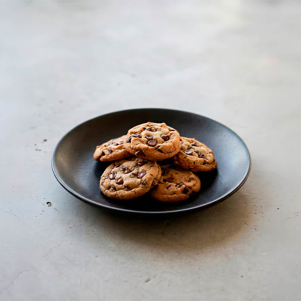 A matte black ceramic dessert plate, featuring several chocolate chip cookies arranged on it. Made in Portugal.