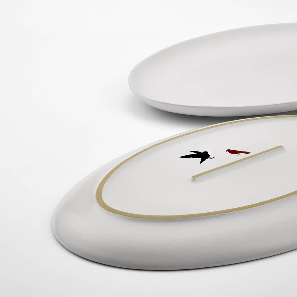 A white ceramic platter with a matt finish, featuring a gold rim and decorative black and red designs.