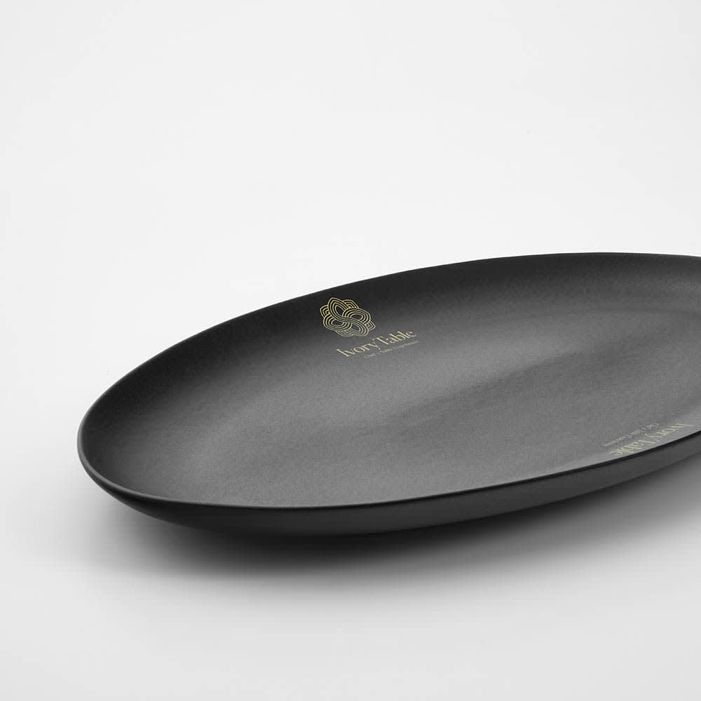 A matte black ceramic platter with an elegant oval shape and a logo. Made in Portugal.