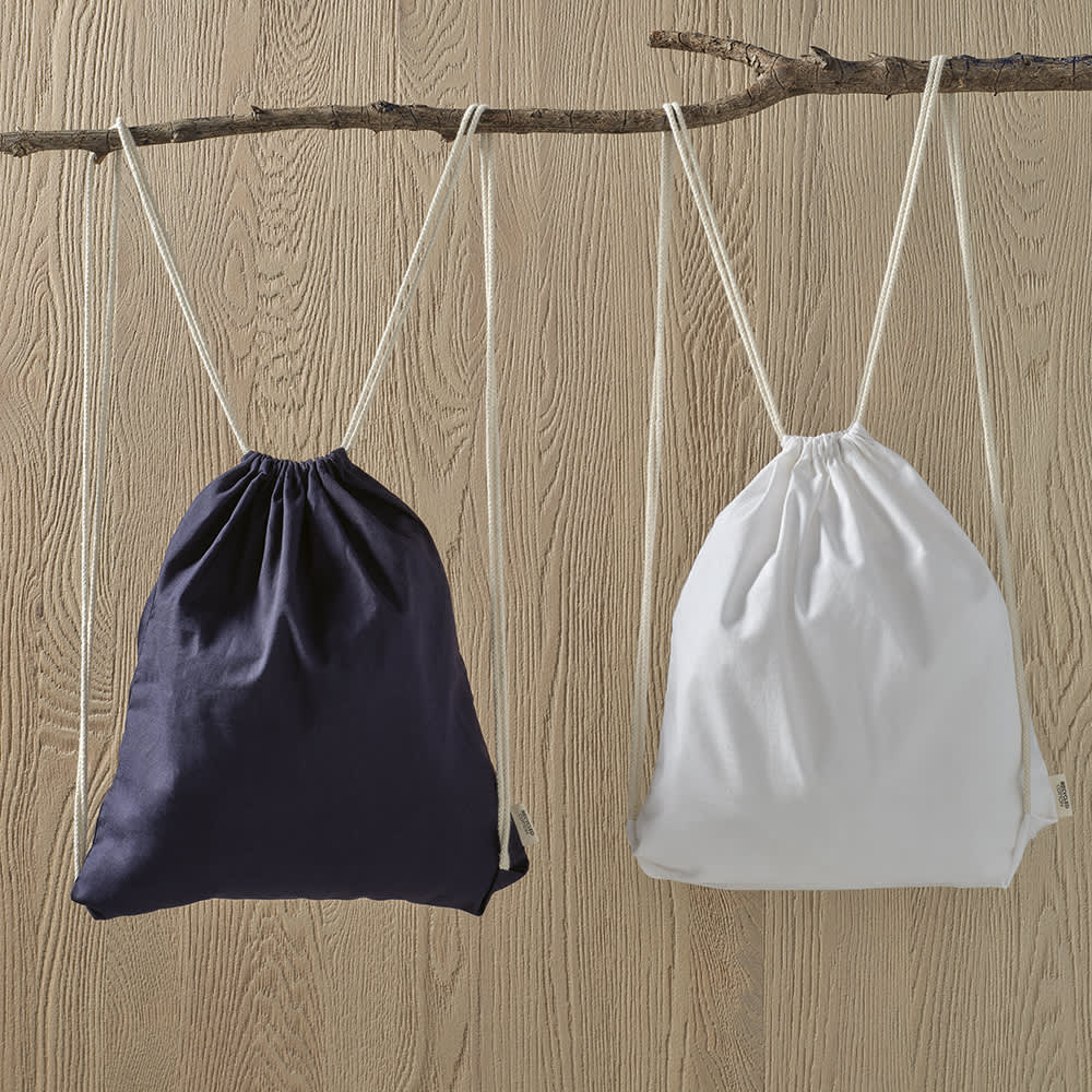 Two drawstring bags in navy blue and white hanging from a branch, featuring rCotton rope straps. Each bag has a logo.