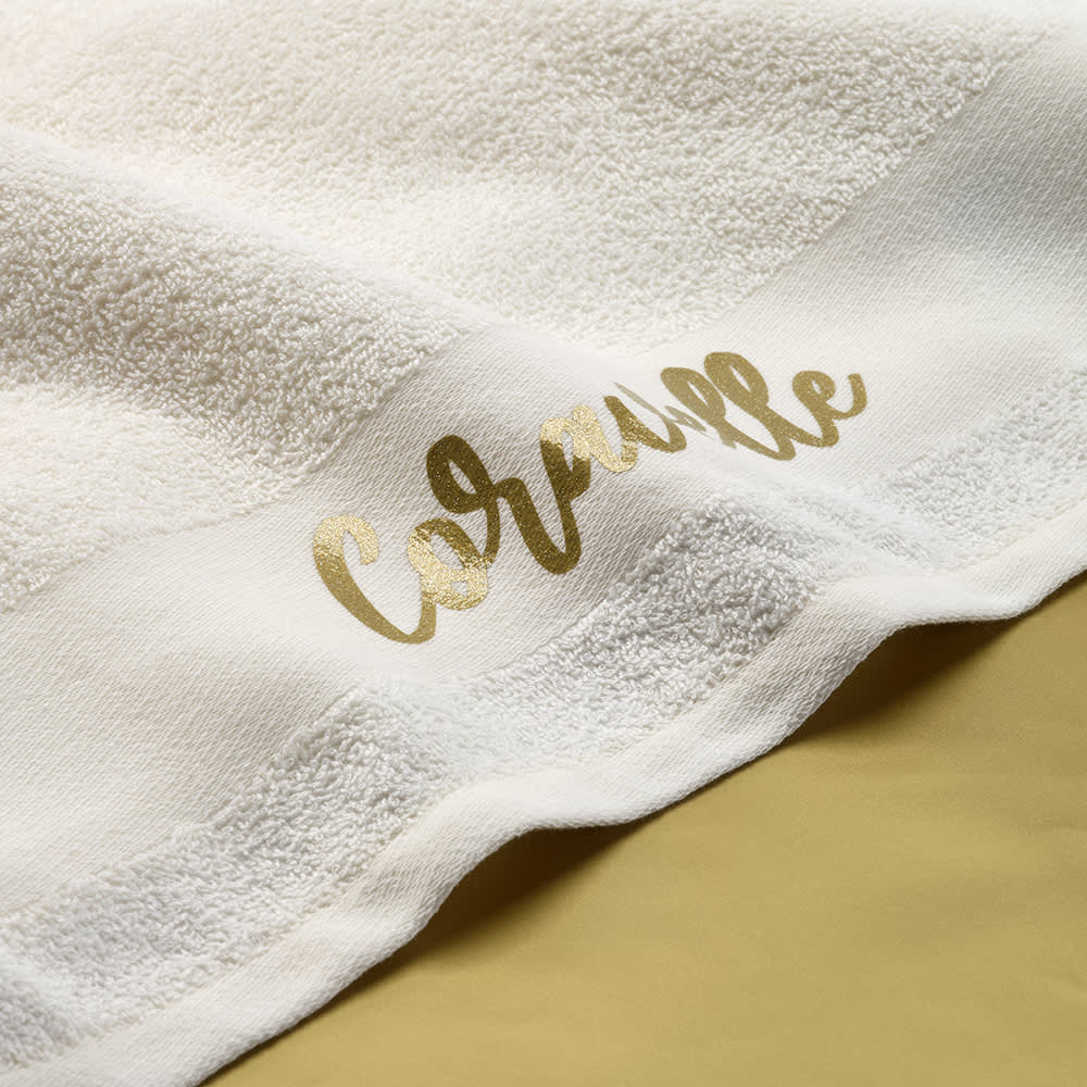 A white cotton towel with a golden logo on one edge, featuring a soft, textured surface.