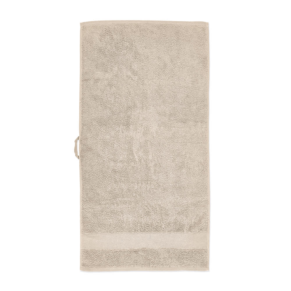 A beige cotton towel with a textured finish, featuring a subtle border and a tag. Contains a logo.