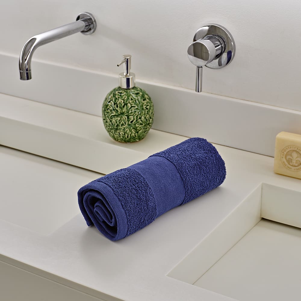 A rolled blue towel placed on a countertop beside a soap dispenser and a bar of soap.