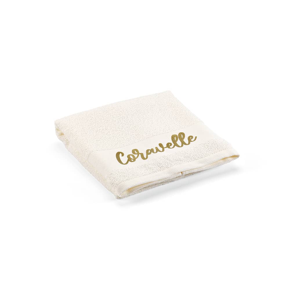 A folded cream towel featuring a gold logo. Made from cotton, with a plush texture.