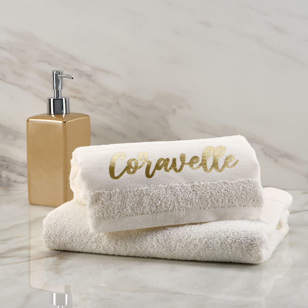 A stack of white towels with a gold design, placed next to a gold soap dispenser on a marble surface.