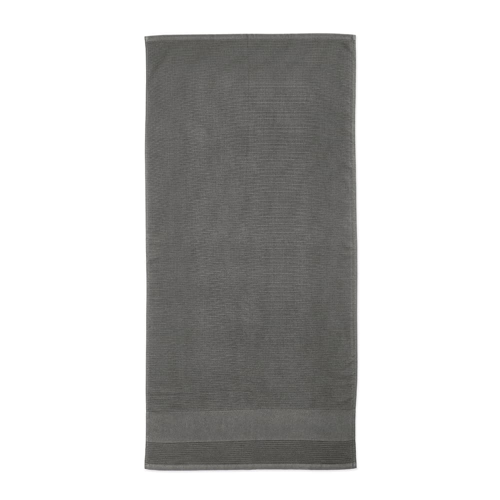 A grey cotton towel with a textured design, featuring a branded logo at the corner. Made in Portugal.