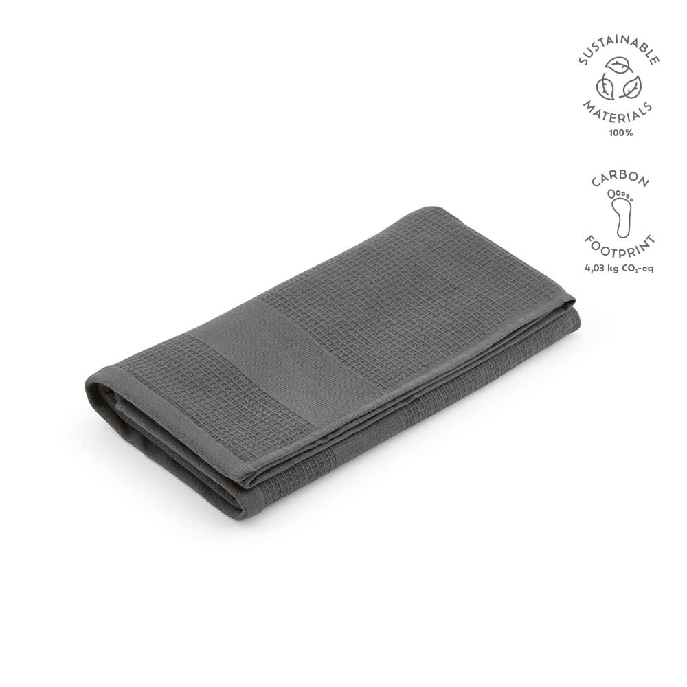 A folded grey towel made from cotton, featuring a textured pattern and a logo. Sustainable materials used.
