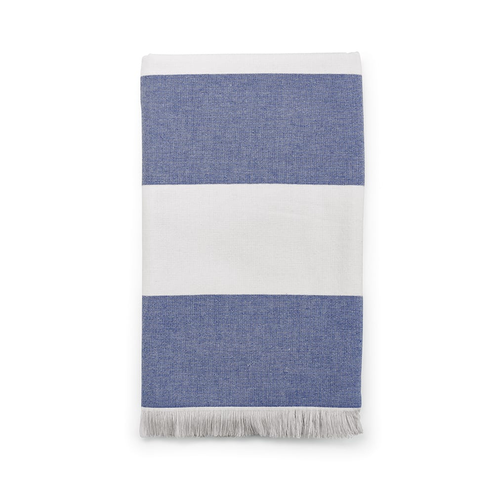 A cotton towel in blue and white stripes, featuring a fringed edge and a logo. Made in Portugal.
