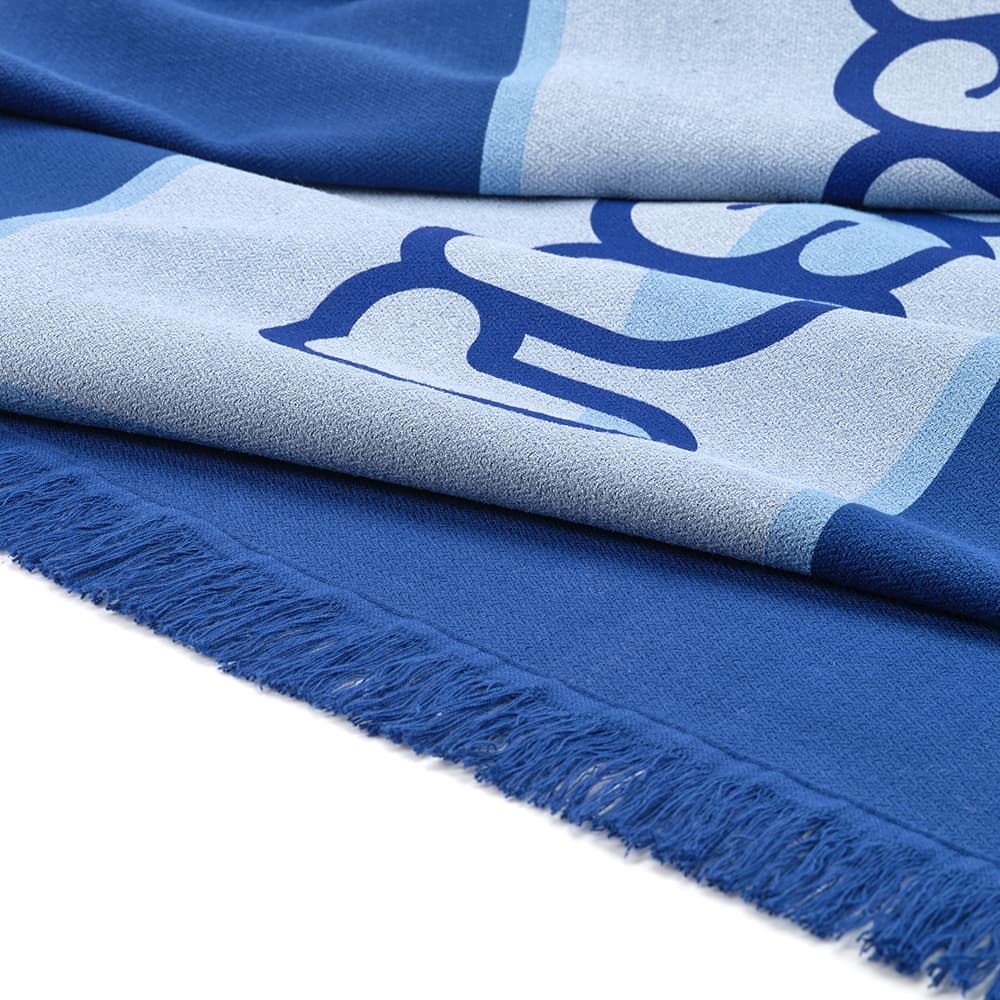 A blue towel with a patterned design and fringed edges, featuring a logo.