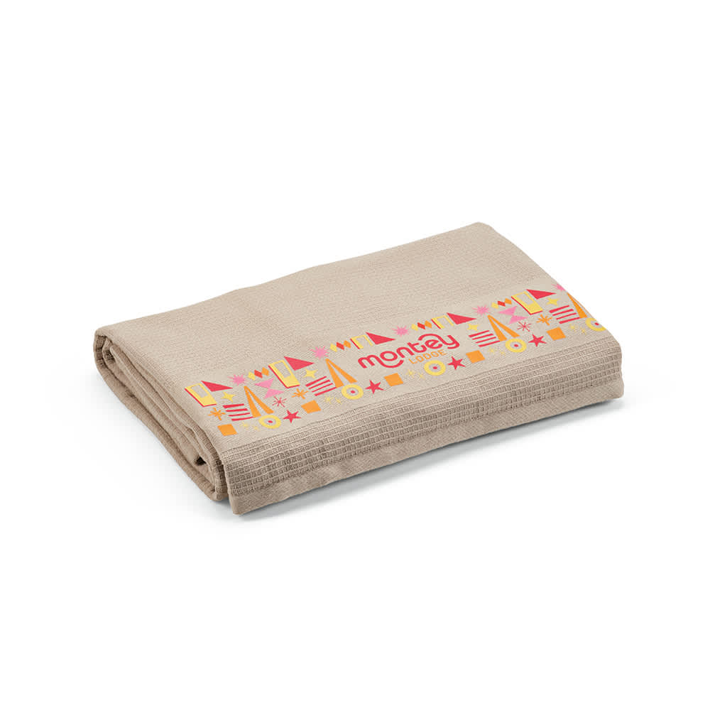 A folded beige towel made from recycled cotton, featuring a patterned edge and a logo.
