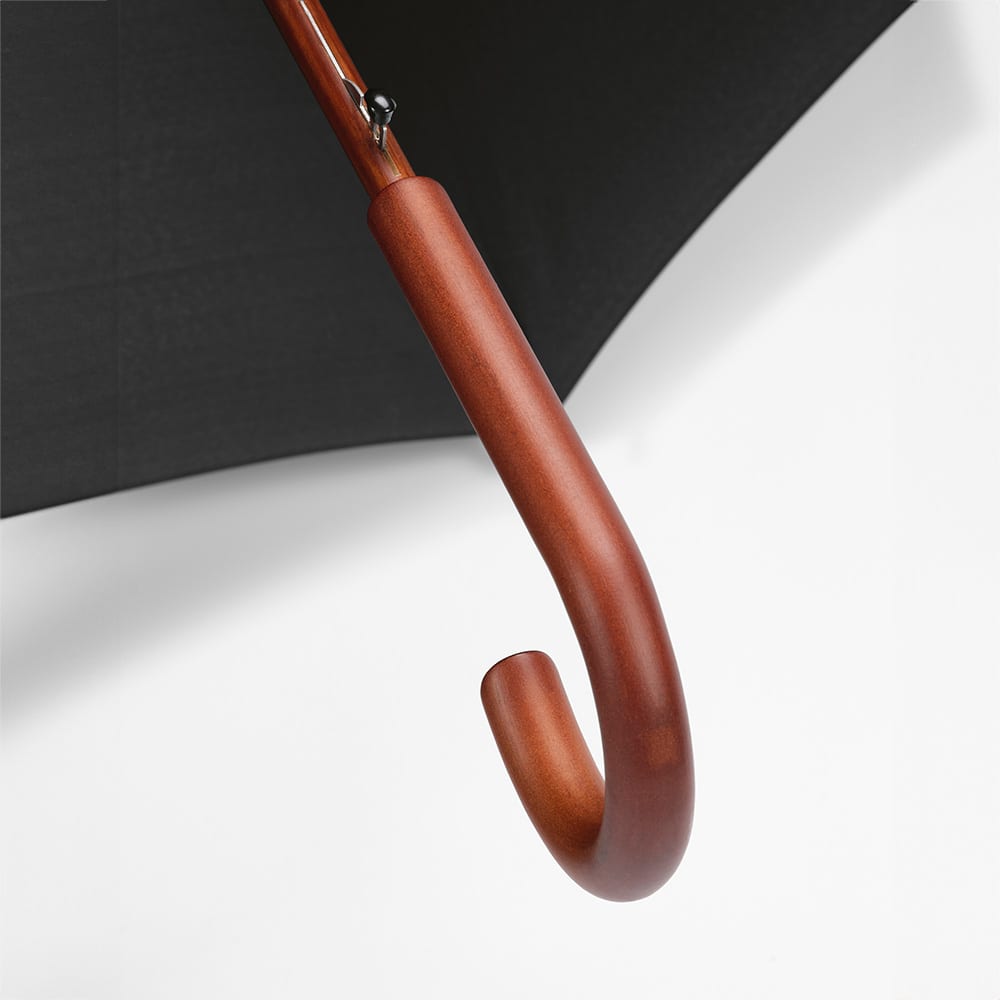 A brown wooden handle with a curved end beneath a black canopy of an umbrella, featuring a logo.