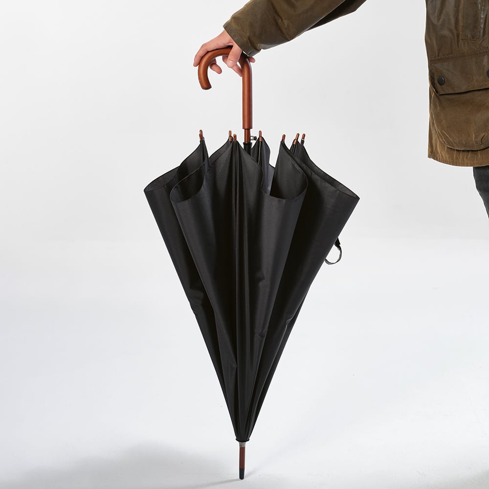 A black windproof umbrella with a brown wooden handle, held by a person wearing a coat.