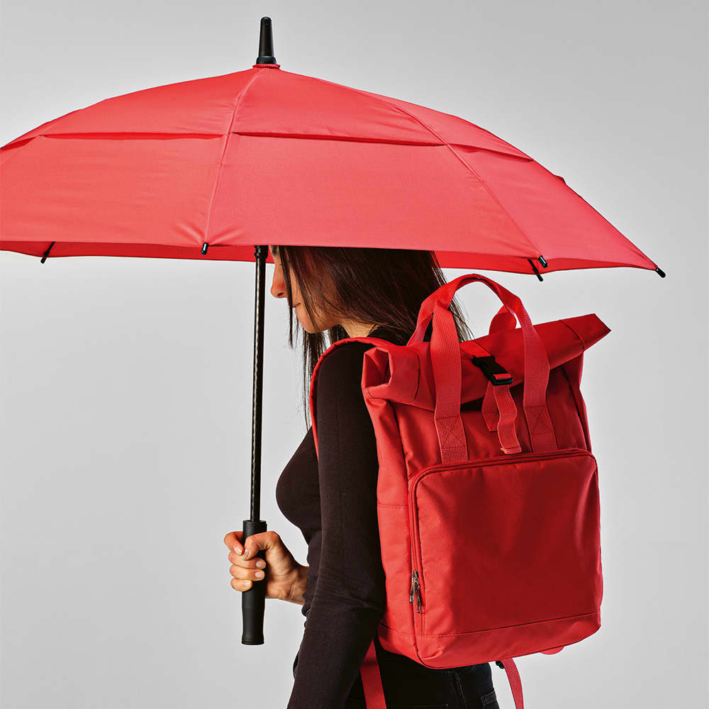 A red umbrella with automatic opening is held by a person wearing a black outfit and a matching red backpack.