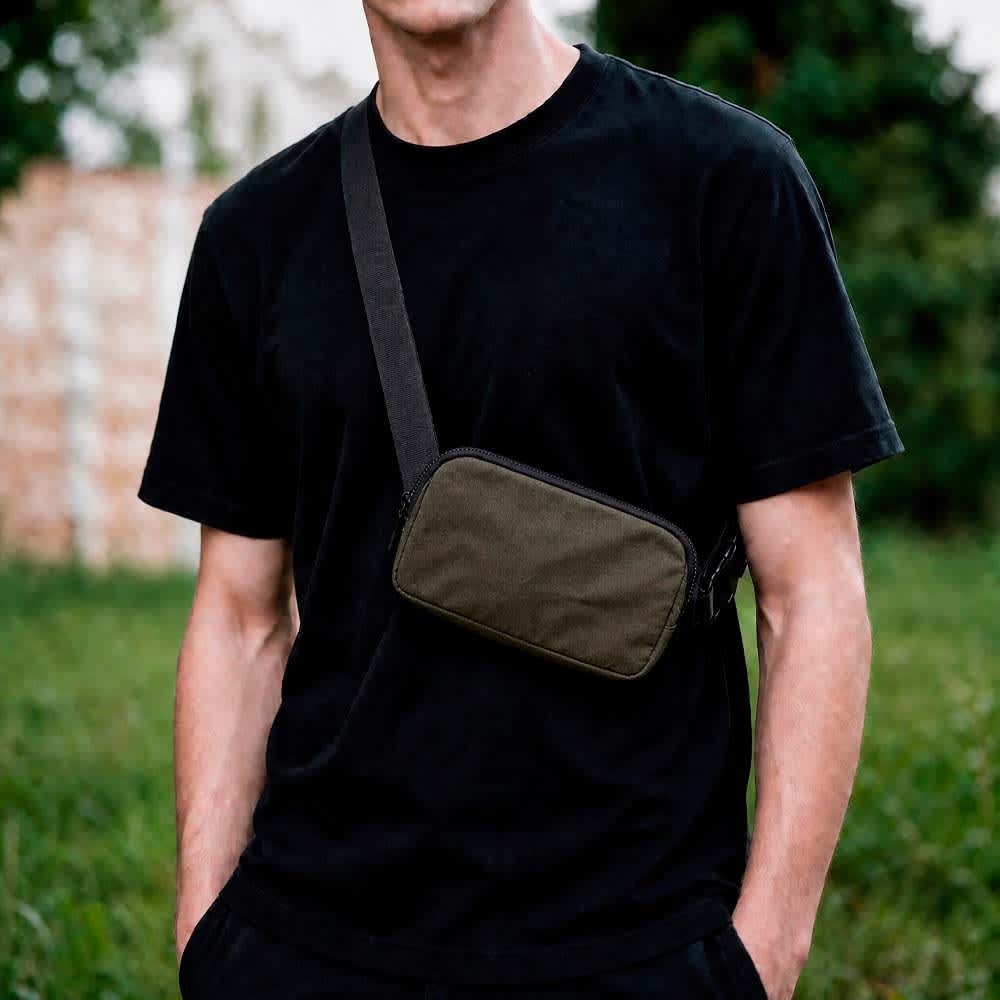 A waist bag in dark green with two pockets and an adjustable strap, worn across a person's body.