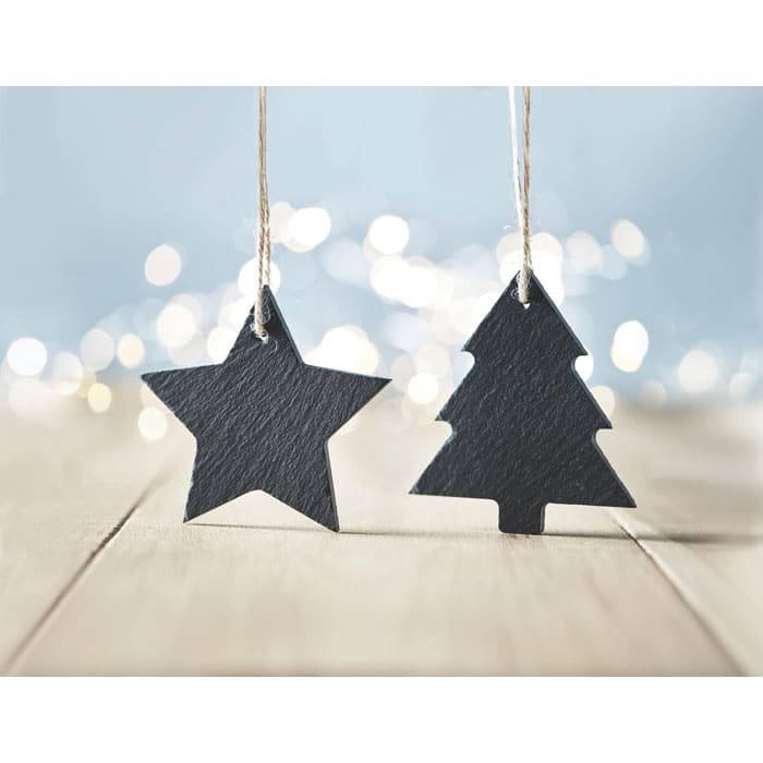 Two black, slate tags shaped like a star and a Christmas tree, hanging from natural twine, against a soft, blurred background.