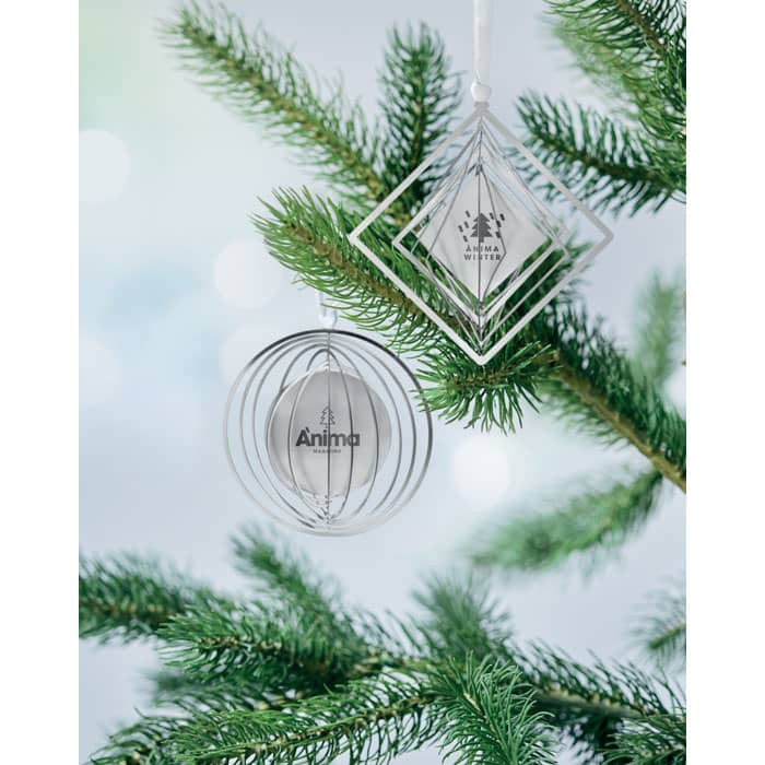 Two Christmas ornaments hang from a pine tree branch. One is a spherical design, and the other is a diamond shape.