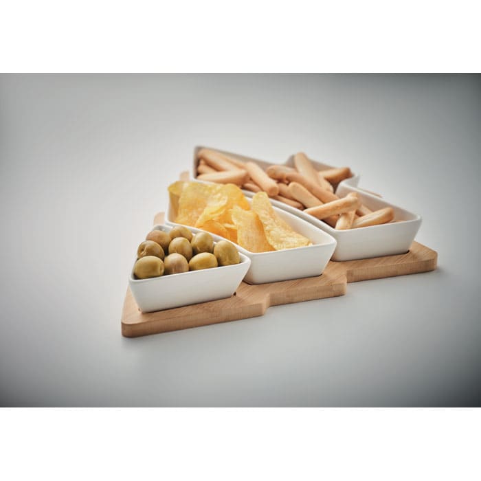 A triangular wooden tray featuring three white bowls filled with green olives, dried fruit, and snacks.