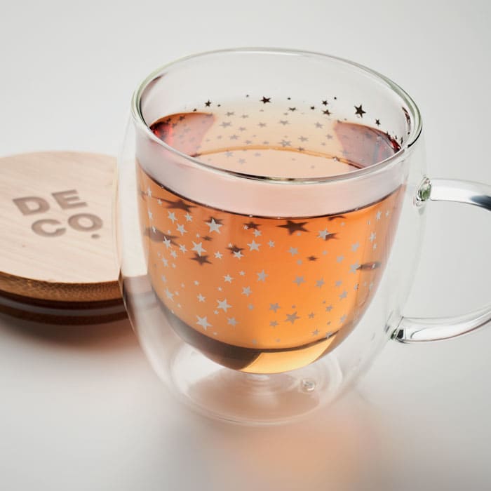 A glass mug with a star-patterned design, filled with amber liquid, sitting on a wooden coaster.