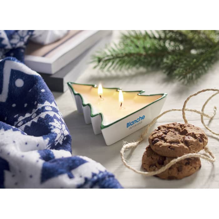 A candle in the shape of a Christmas tree, featuring three wicks, beside cookies and a patterned blue cloth.