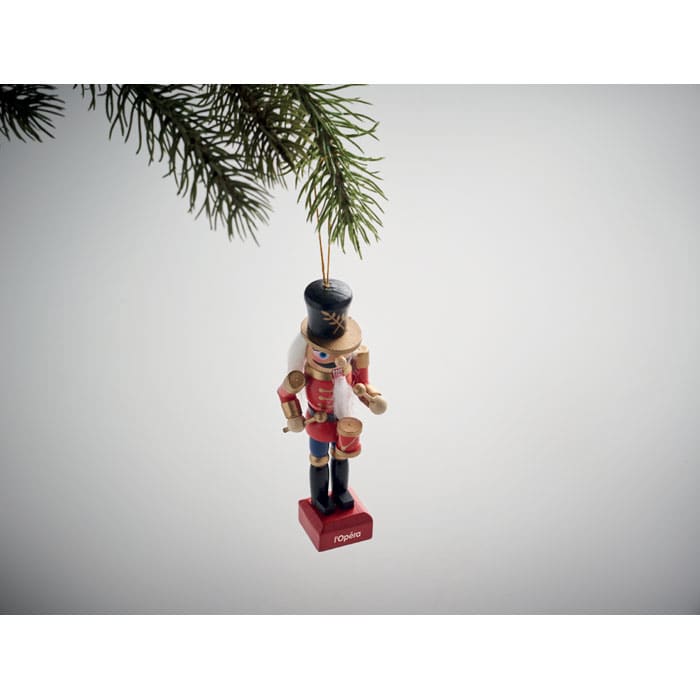 A wooden nutcracker ornament in red and blue, hanging from a pine branch.