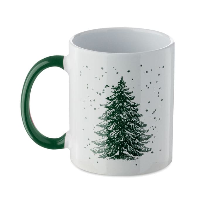 A white mug with a green handle featuring a black and green illustration of a Christmas tree on a speckled background.