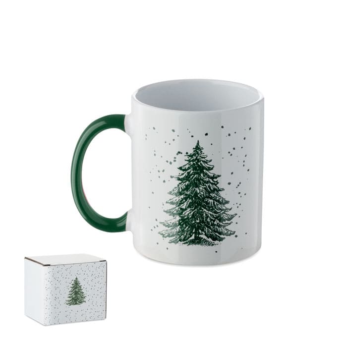 A drink mug with a green handle featuring a decorative tree design and a small gift box.