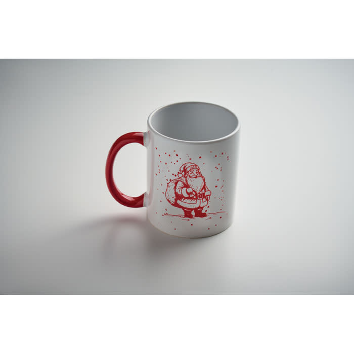 A white mug with a red handle featuring a festive illustration in red. The mug has a logo on it.