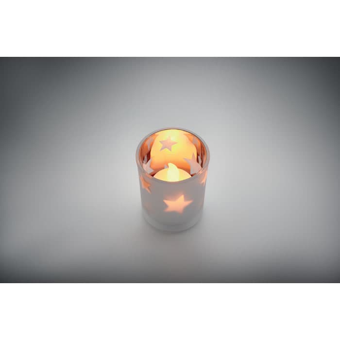A candle holder featuring star cut-outs, illuminated from within, sitting against a subtle grey background.