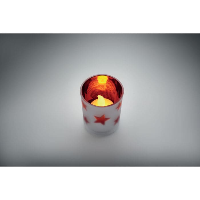 A candle holder with a glossy red interior and white exterior featuring red stars. It holds a flickering candle.