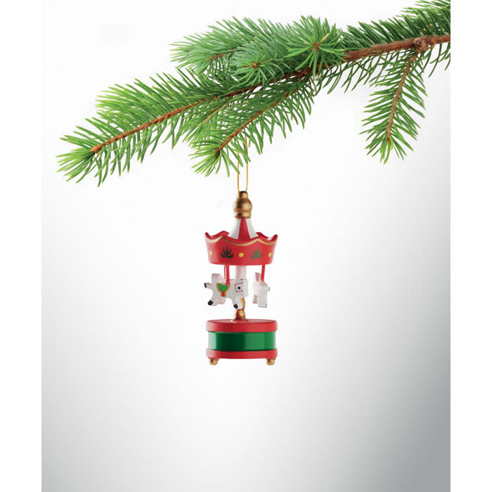 A decorative carousel ornament in red and green hangs from a pine branch, featuring playful animal figures and festive details.
