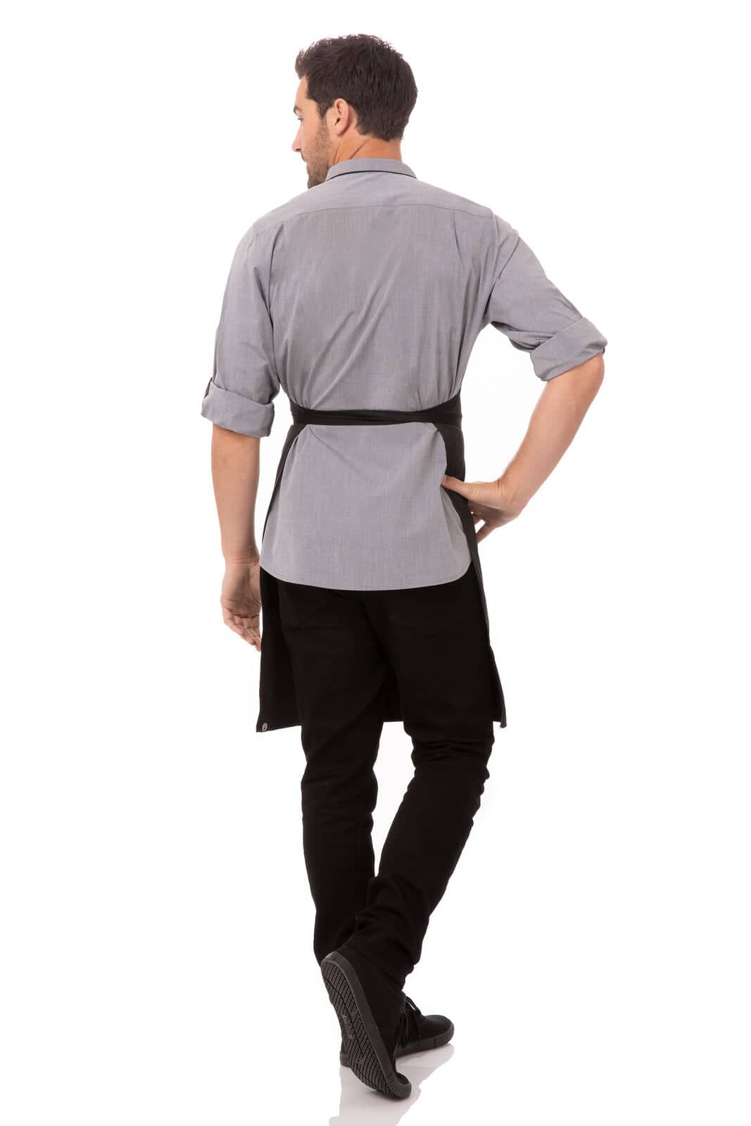 A man wearing a grey shirt and black bib apron with contrasting ties, standing with his back to the camera.