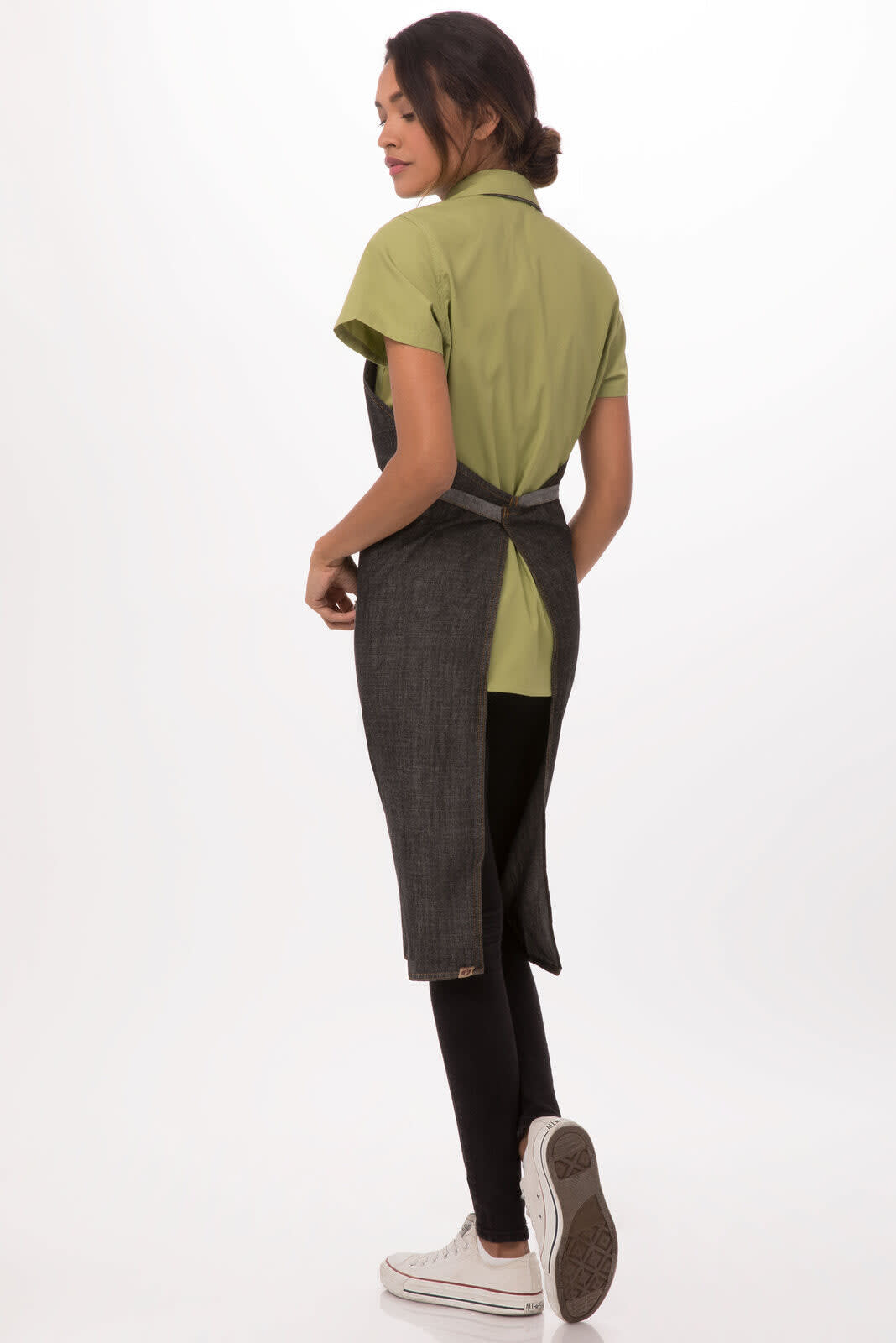 A woman wearing a green shirt and a black Manhattan Bib Apron from the back, featuring a tied waist.